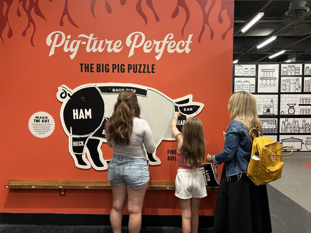 An adult and two kids put together a pig puzzle on the wall.