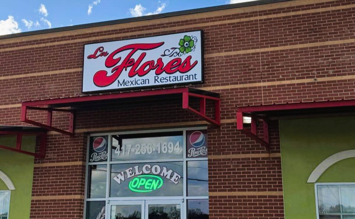 the outside of a brick restaurant building, with a sign white background and red text reading "los Flores Mexican Restaurant."