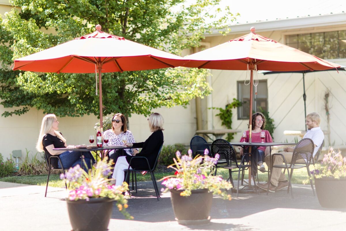 People sit at tables beneath umbrellas on a sunny day.