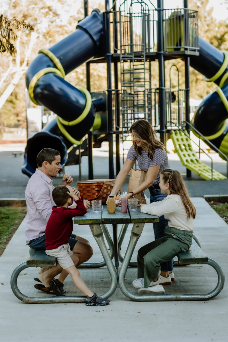 A family sits at a picnic table at a park.