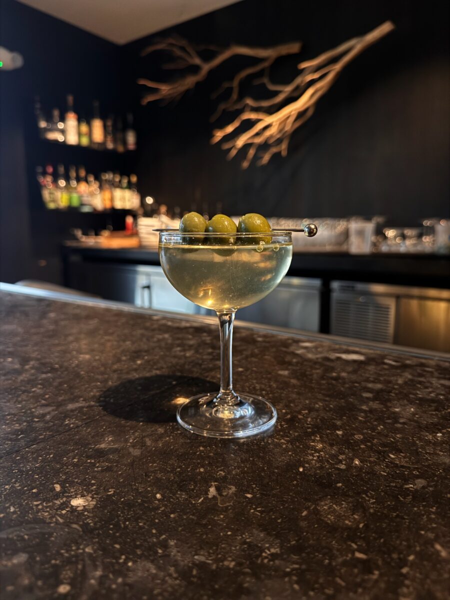 A cocktail with three olives on a bar in Vicia.