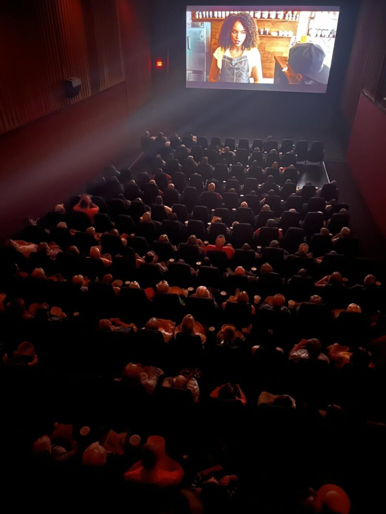 A crowd watches a screen at a movie theater.