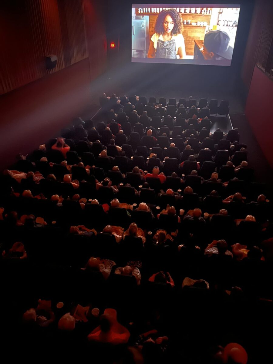 A crowd watches a screen at a movie theater.