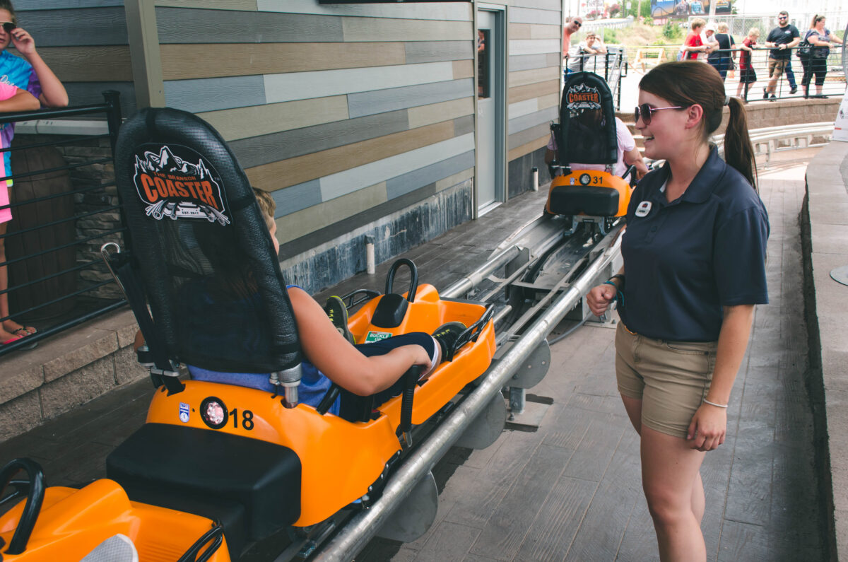 An attendee talks to a roller coaster rider in an orange car.