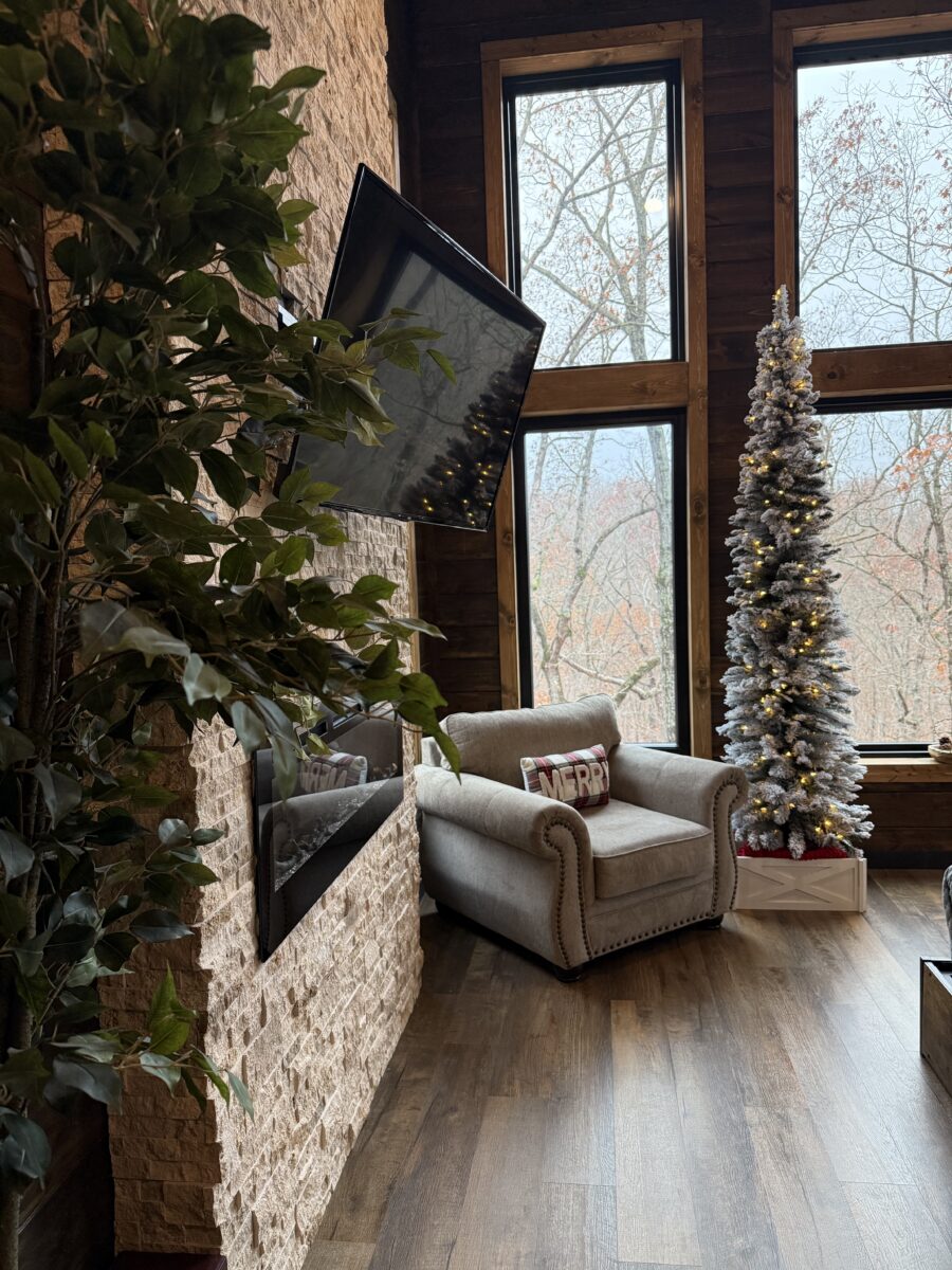 The corner of a room with a chair, stone walls and a TV and Christmas tree.