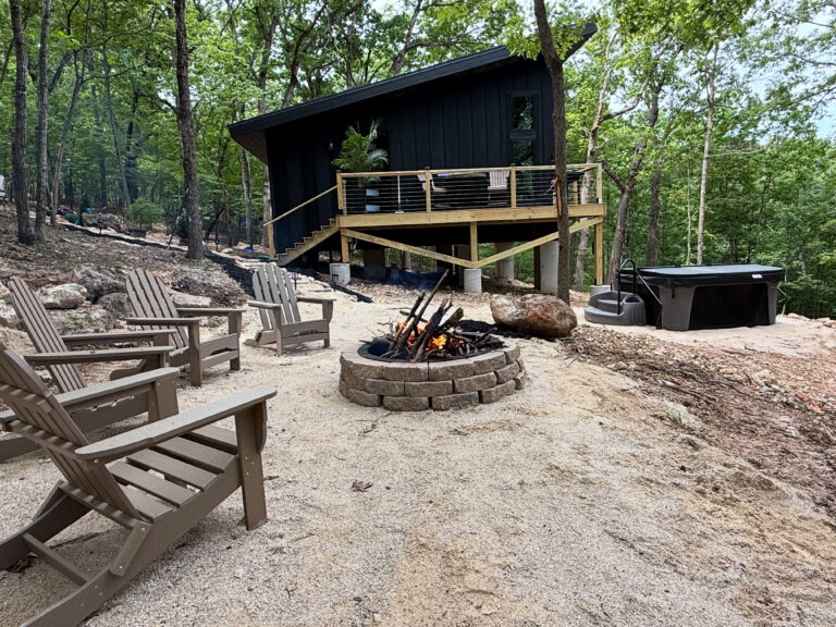 The exterior of a treehouse with chairs and a fire pit.