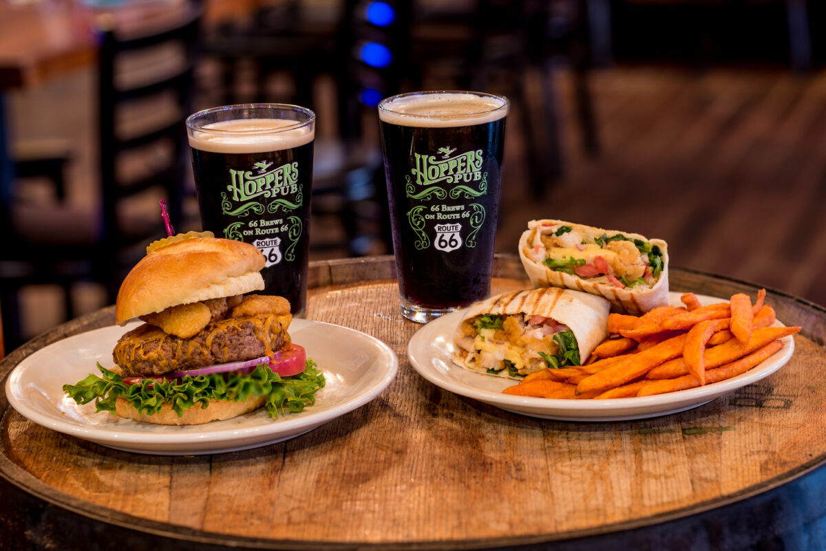 Two glasses of beer and plates of burger and fries.