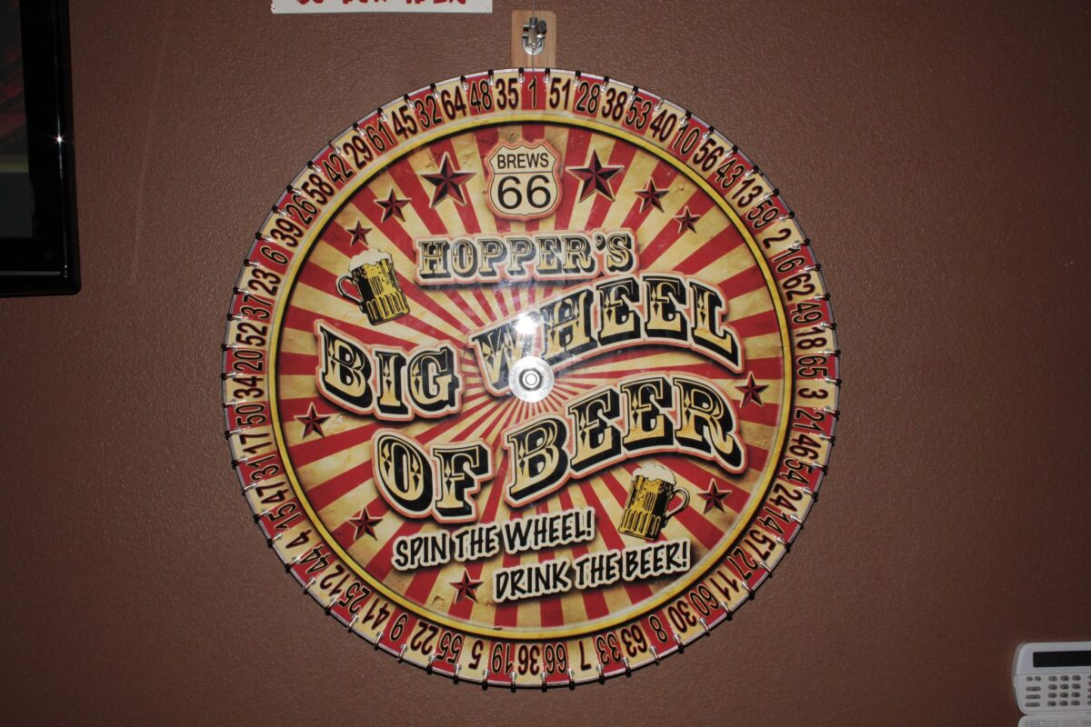 A round, yellow and red sign advertising Hoppers Big Wheel of Beer.