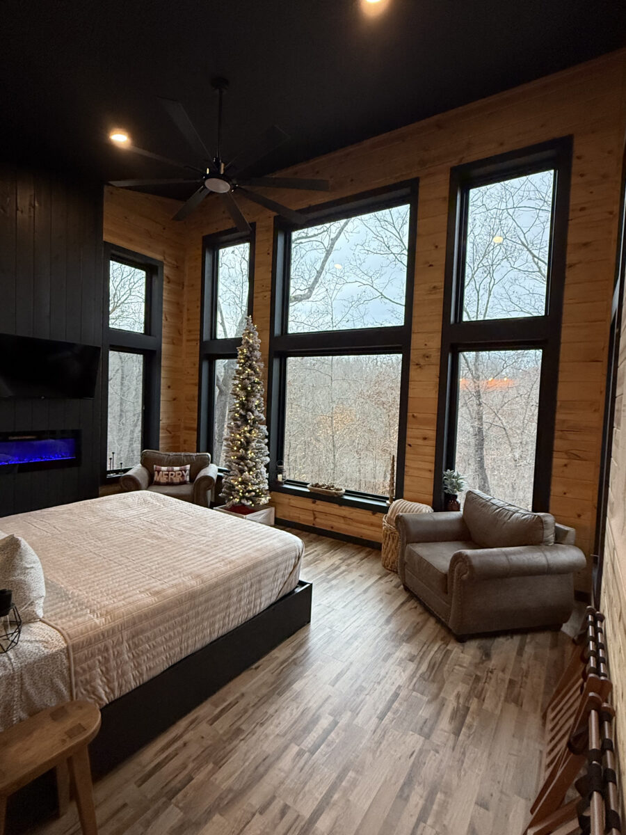 The interior of a treehouse bedroom with a large bed and picture windows.