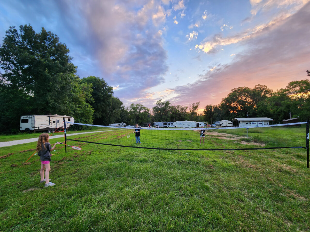 People playing sports outside under a vibrant blue and orange sky, near campers.