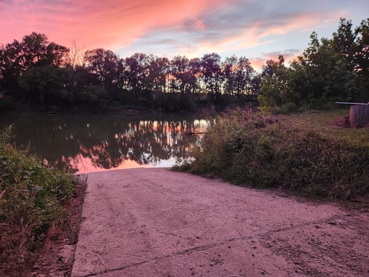 A boat ramp down to the water under a colorful sky.