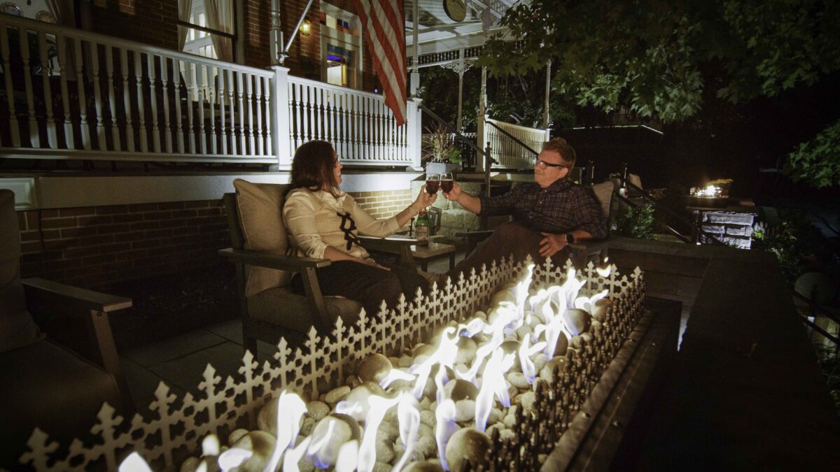 Fall in Love with Parkville: Couple enjoying wine next to a fire pit at night outside the Main Street Inn, with cozy autumn ambiance and glowing flames