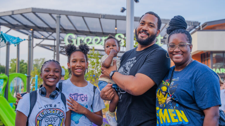 Two adults and three children pose for a photo during an outdoor farmers market event.