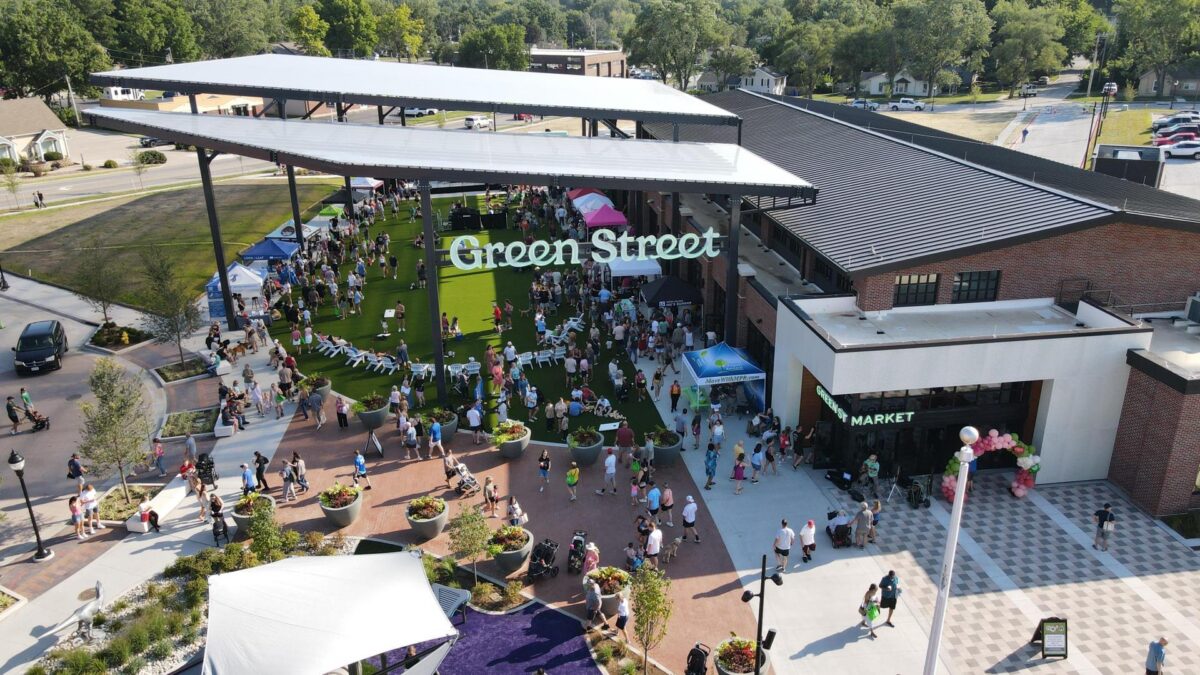 People walk around an outdoor farmers market venue on a sunny day under an awning that reads "Green Street."
