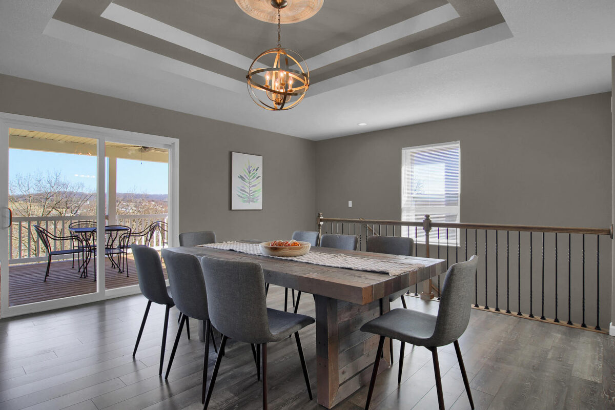 The interior of a modern vacation rental home, with a table and several chairs beside a patio and under a lighting piece.