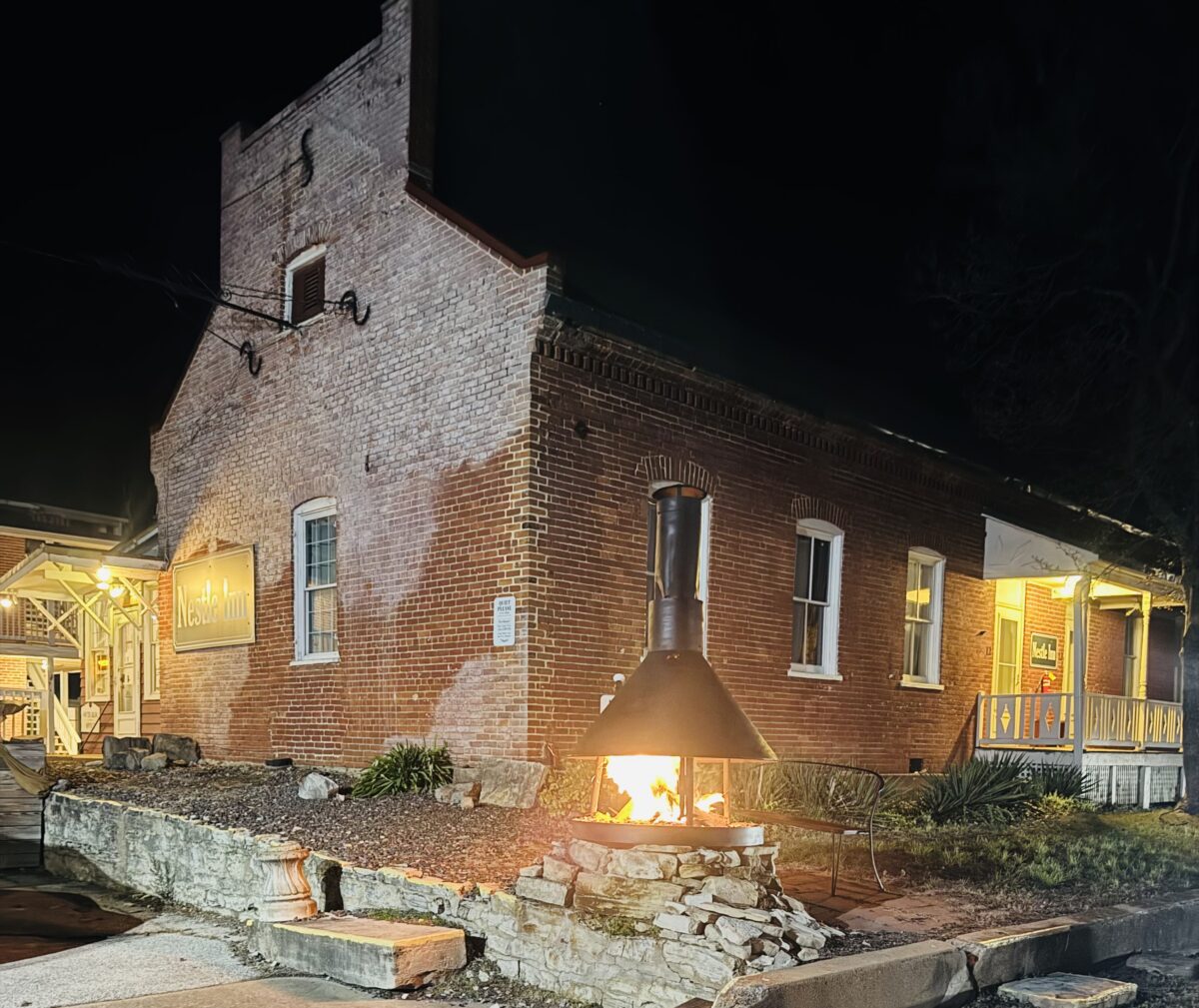 The outside of a brick building at night, lit by a fire pit.