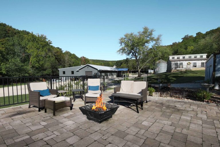 Patio furniture outdoors on a stone tiled surface with a lit fire pit in the middle.