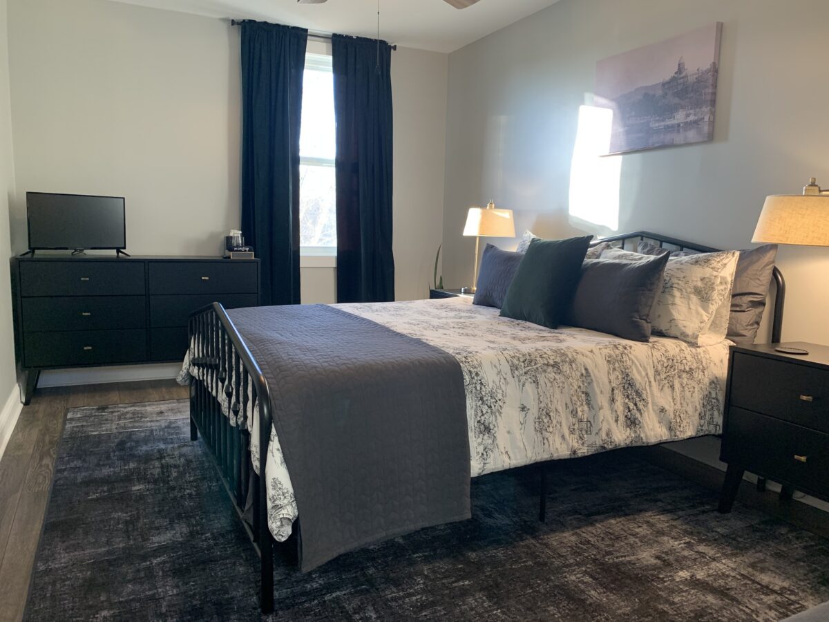A bedroom with curtains, a rug and a large bed.