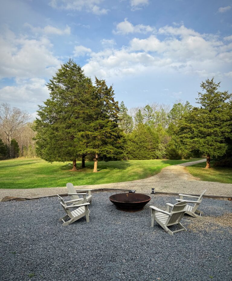 A fire pit and white chairs outside of a rental house.