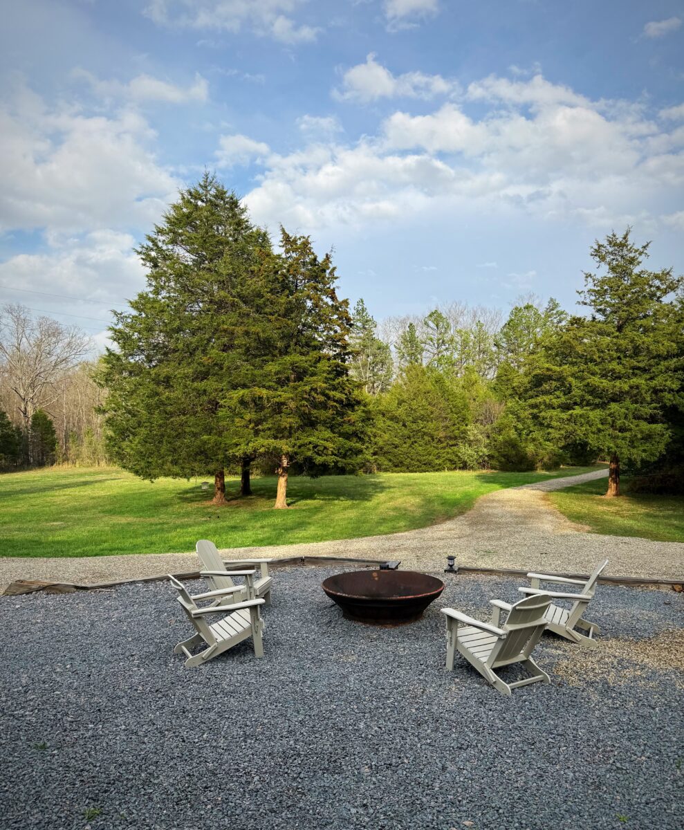 A fire pit and white chairs outside of a rental house.