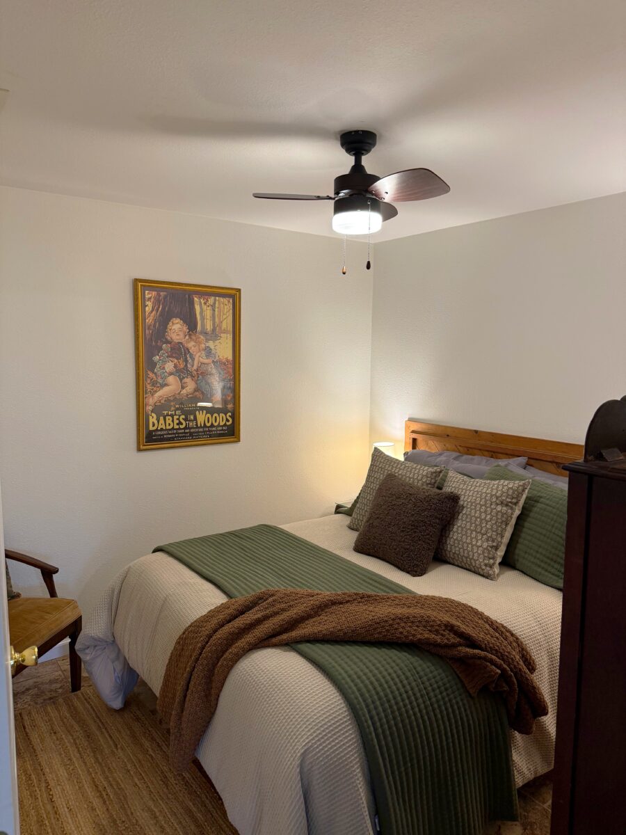 A furnished bedroom with a bed, ceiling fan, furniture and artwork.