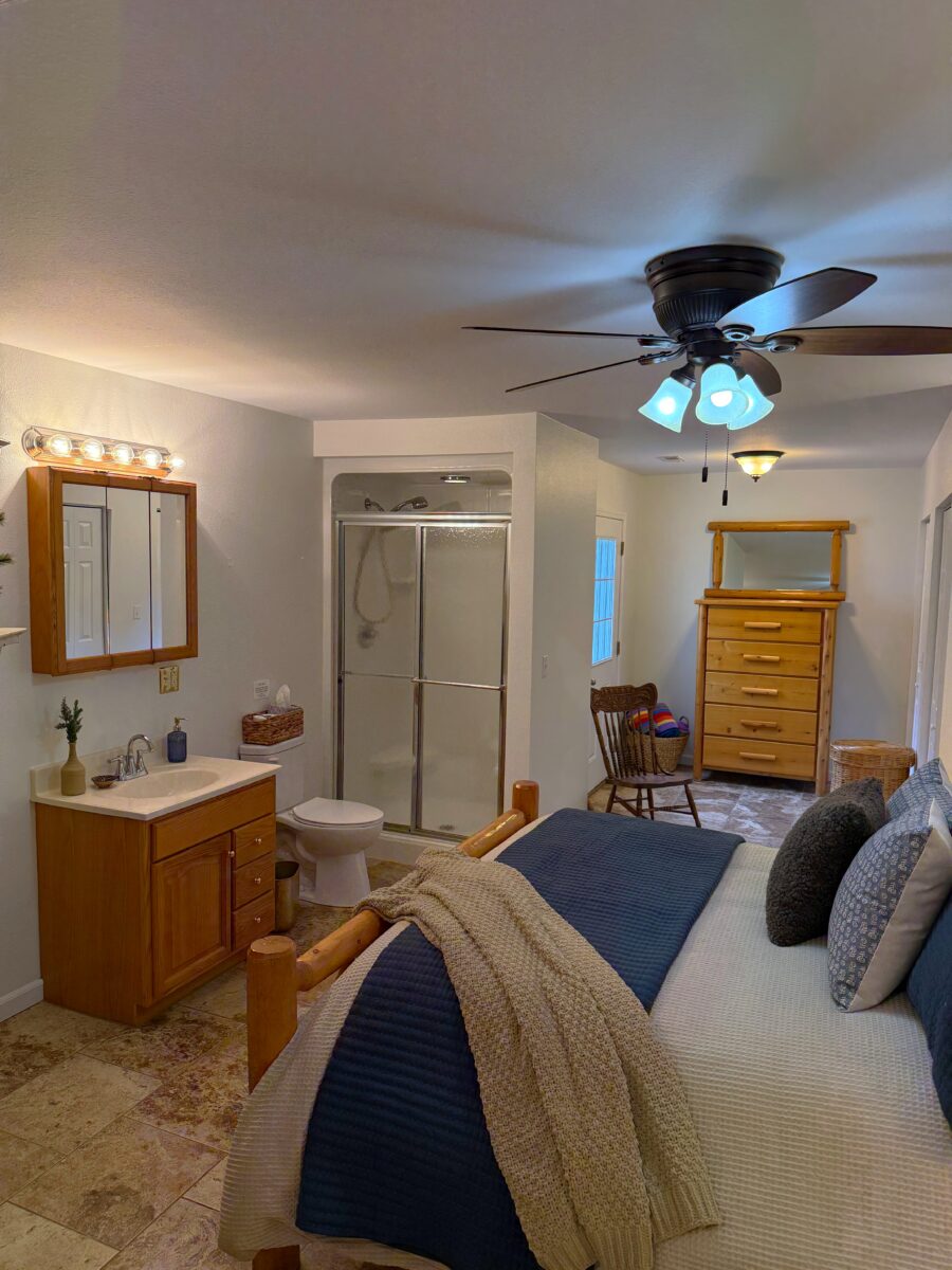 A furnished bedroom with a bed, ceiling fan, furniture and artwork.