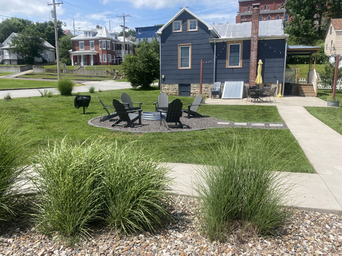The outside of a cabin with chairs in a circle in the yard.