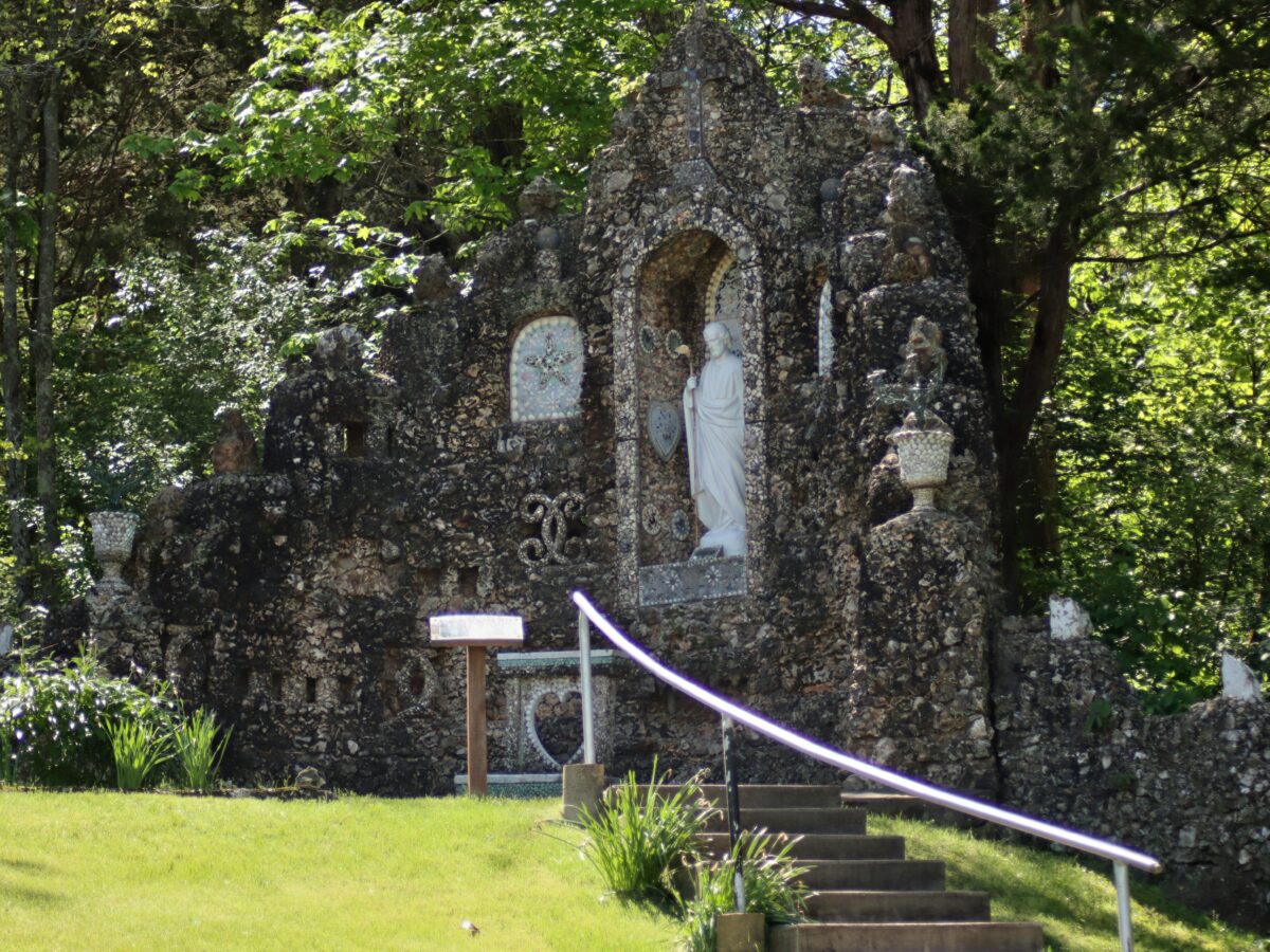 Stone structures and sculptures outdoors amid grass and stairs.