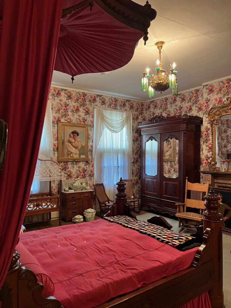 The Thomas Lawson Price Bedroom, with historical wallpaper and a red made bed.