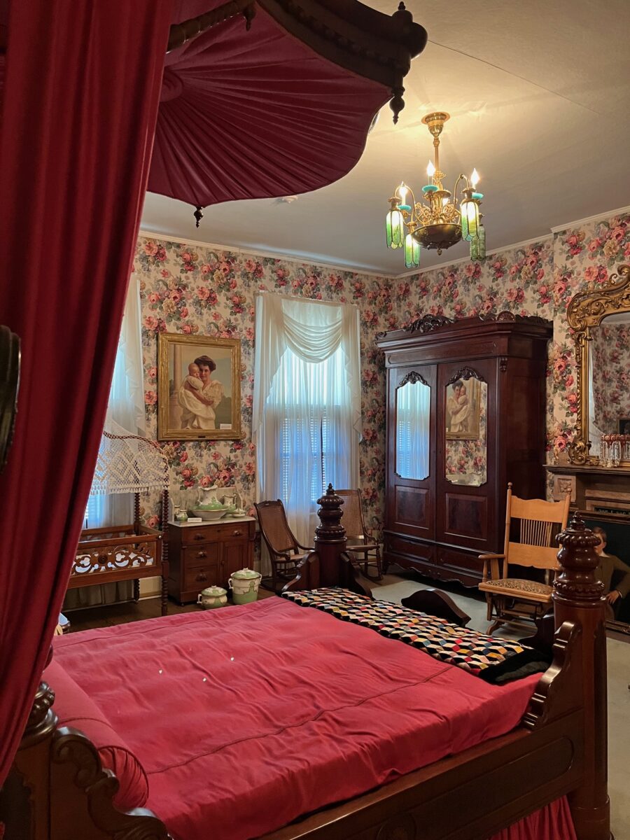 The Thomas Lawson Price Bedroom, with historical wallpaper and a red made bed.