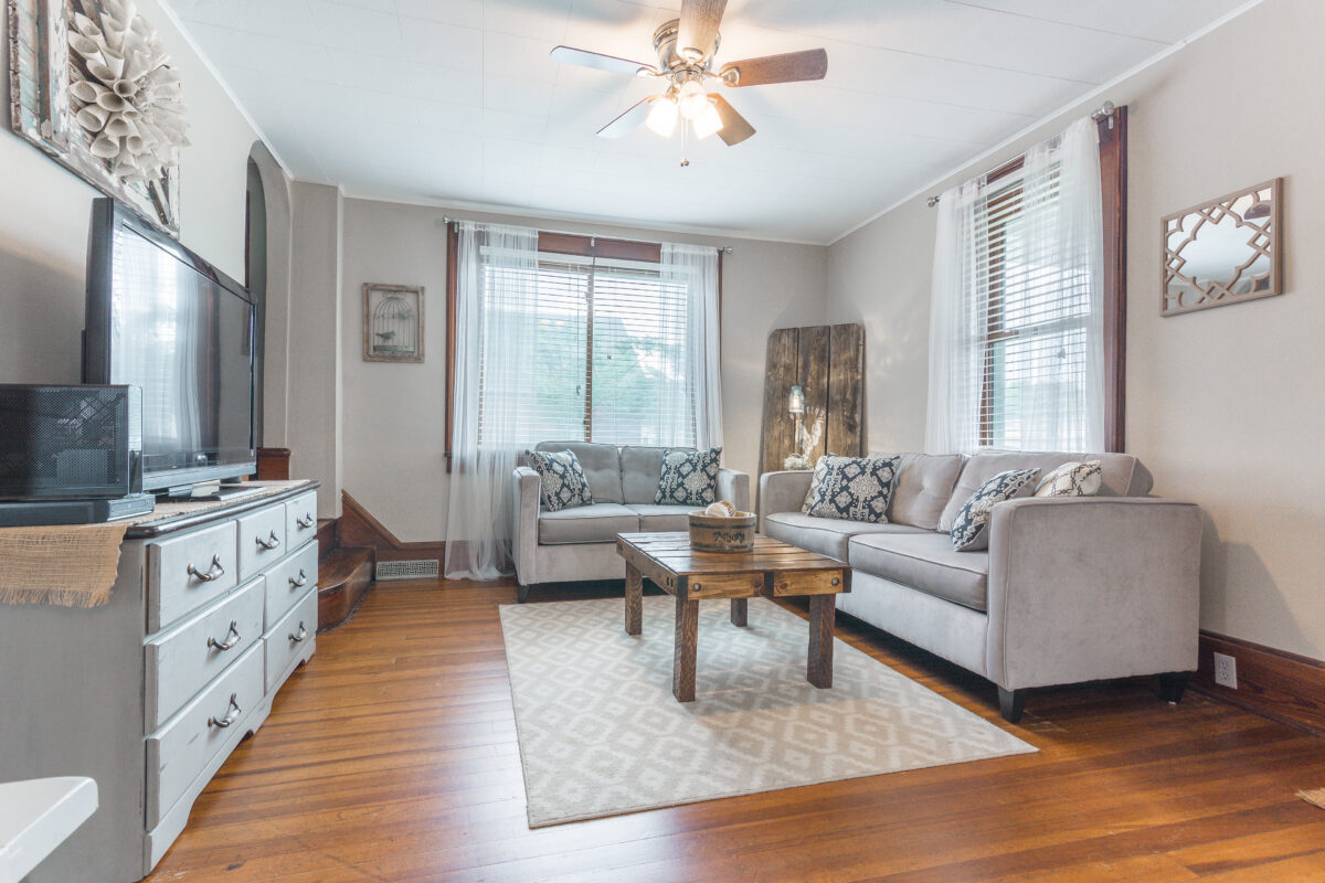 A furnished cottage living room with a couch and love seat, table, and a dresser with a television on top.