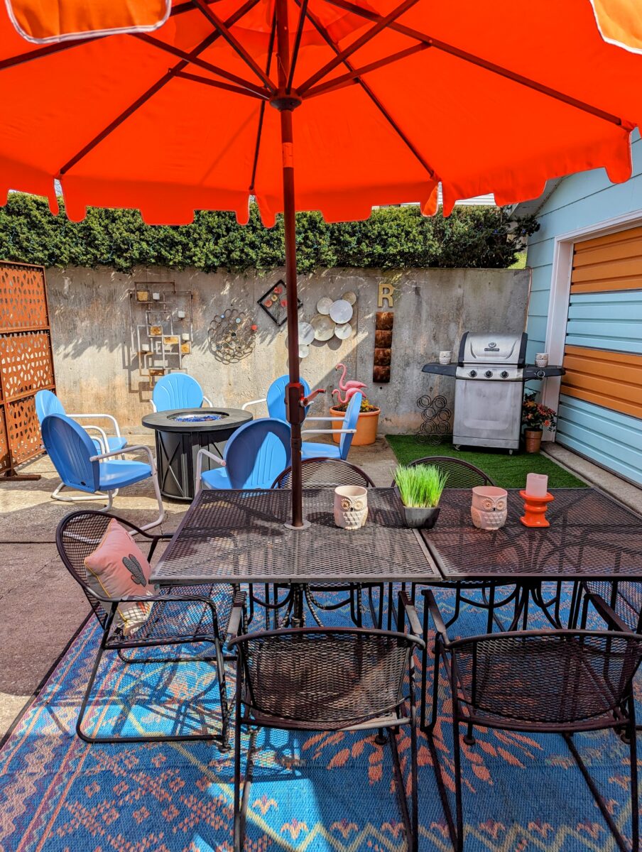 An outdoor patio with a bright orange overhead umbrella and colorful rugs and chairs.