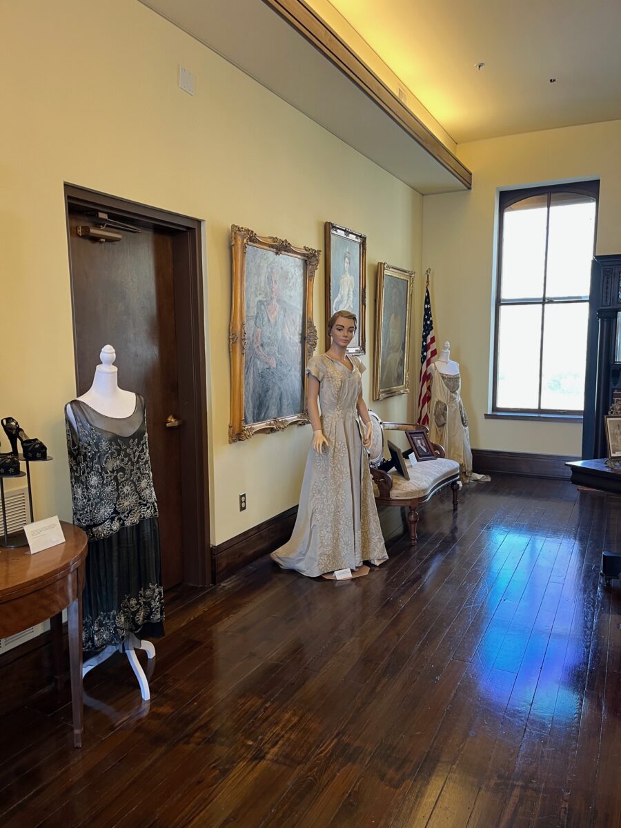 A woman in a dress among mannequins holding Missouri First Ladies' Gowns.