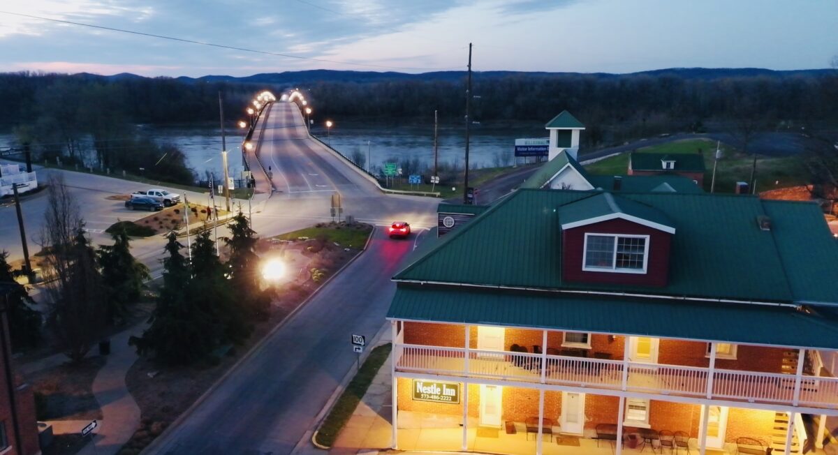 An aerial view of a town, with budlings, roads and water beneath the bridge.