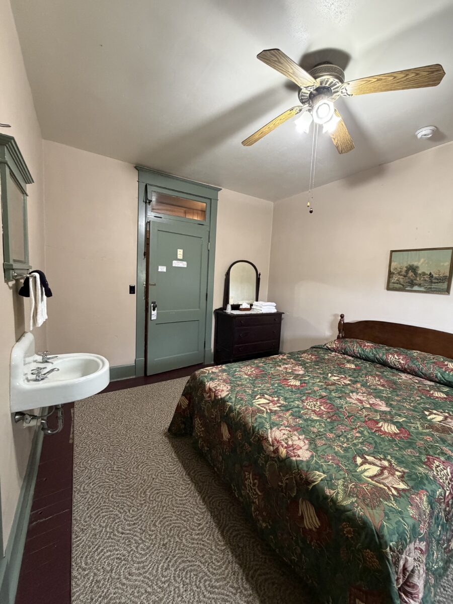 The bedroom of a lodge, with a bed, ceiling fan and sink.