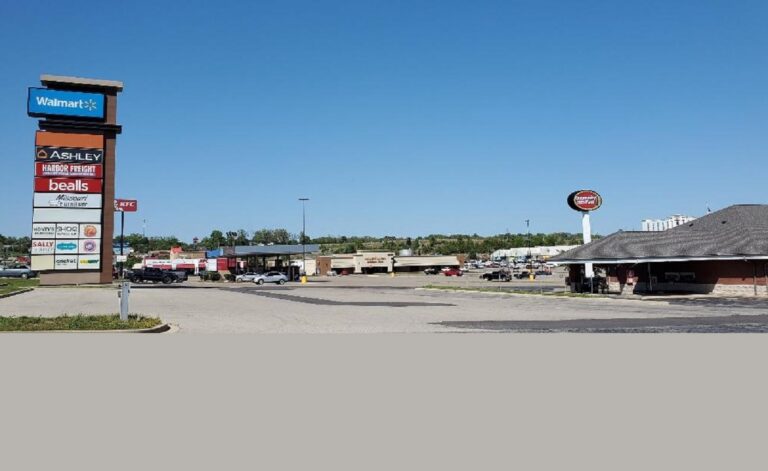 An exterior view of a shopping center from the road, depicting signs and storefronts from afar.