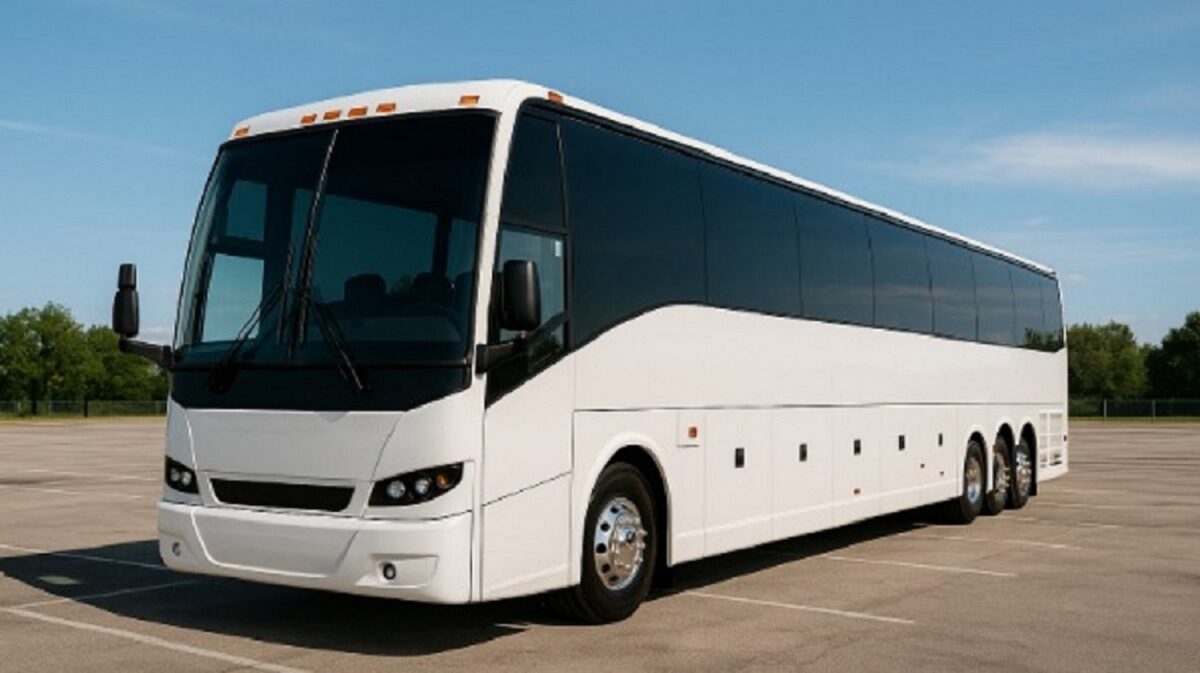 A large white bus with dark windows on concrete beneath a blue sky.
