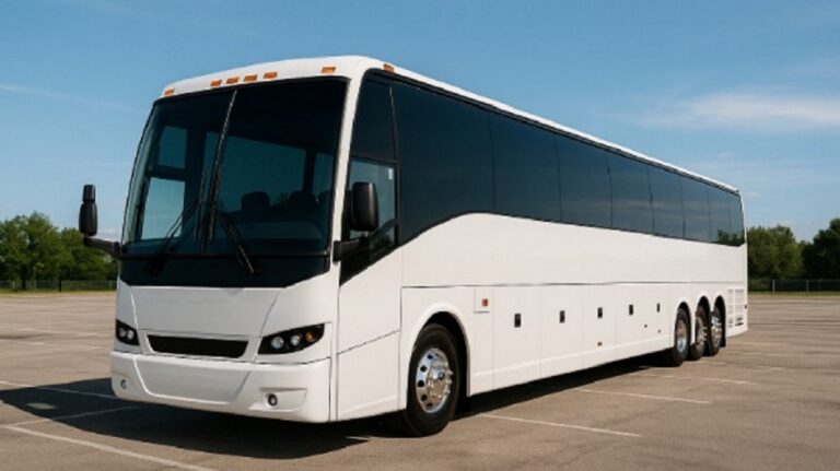 A large white bus with dark windows on concrete beneath a blue sky.