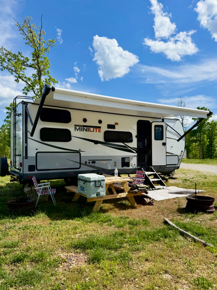 A camper parked near bright green grass and clouded blue skies.