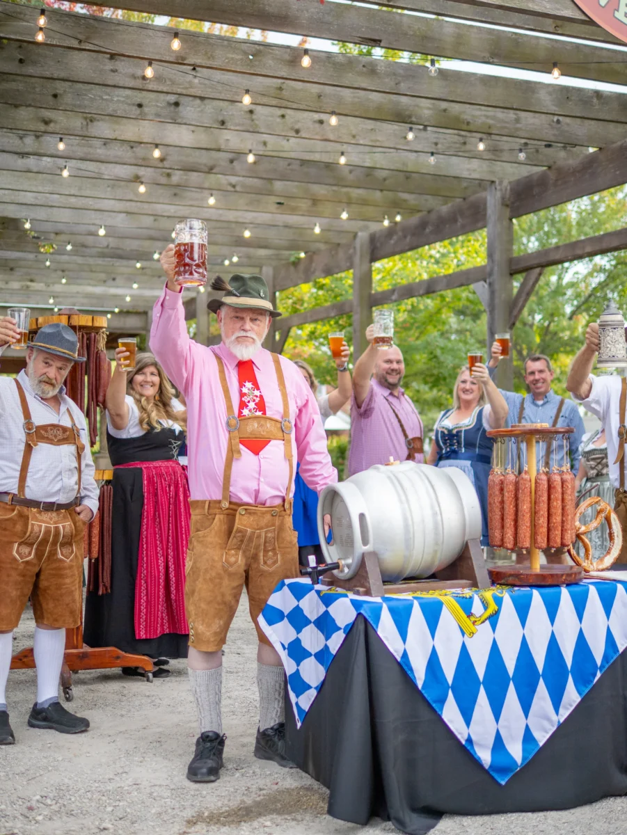 Several people in bright, traditional German dress raise beer mugs.