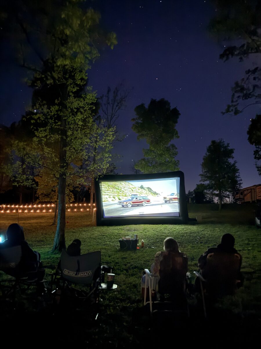 Several people outdoors watching a movie on a screen.