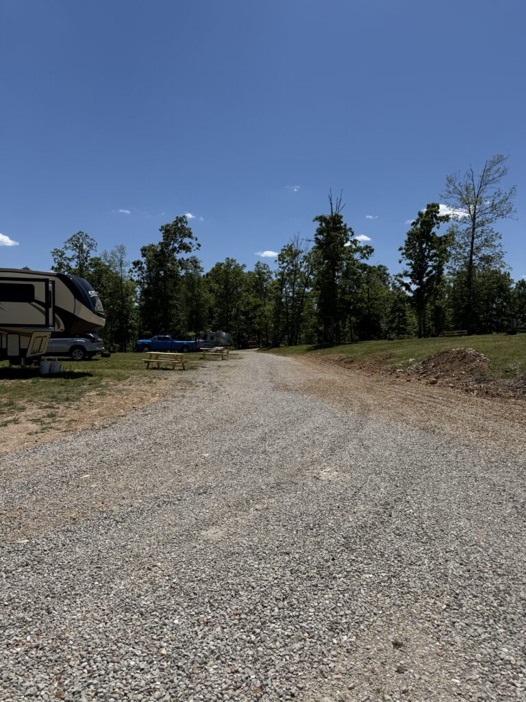 A gravel road toward trees and bright blue sky.