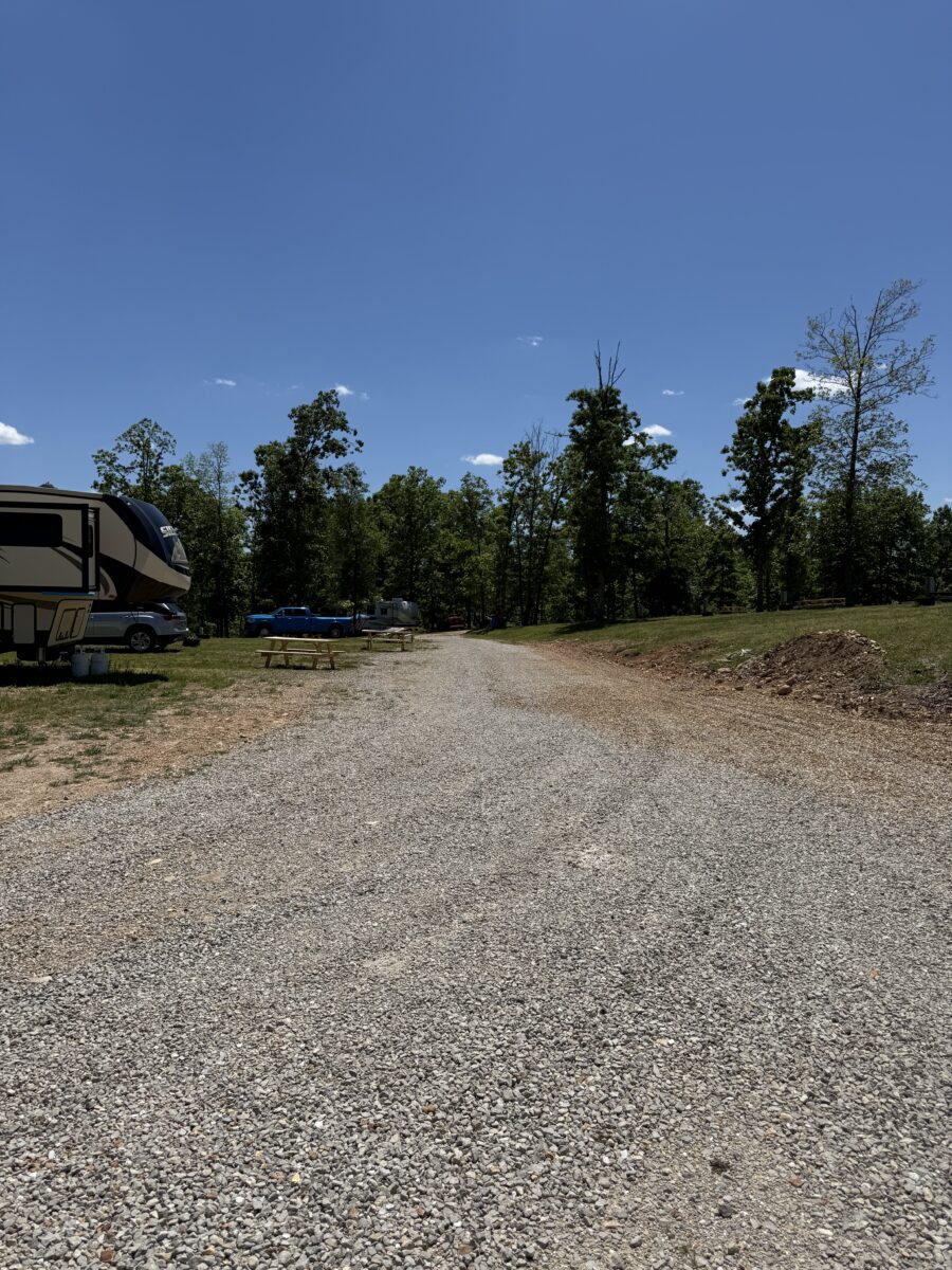 A gravel road toward trees and bright blue sky.