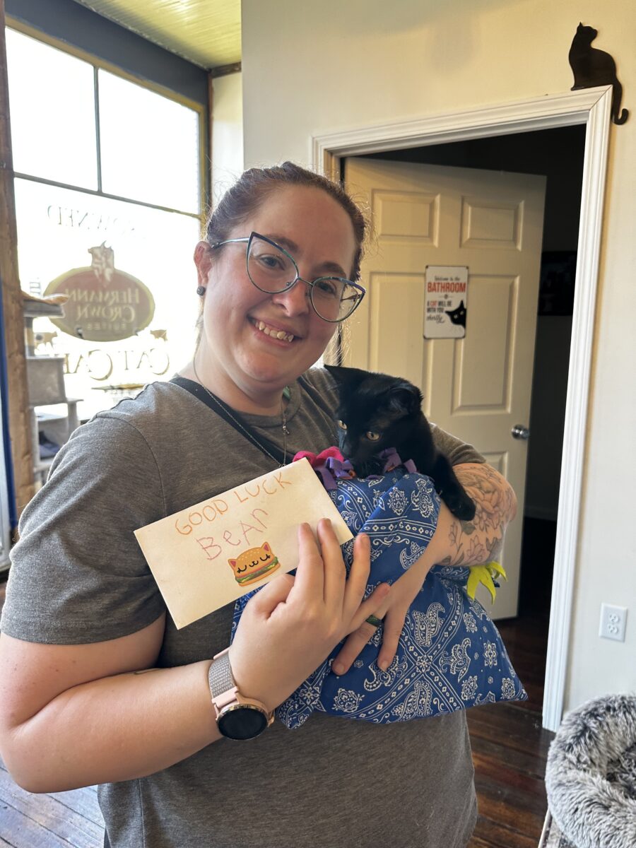 A woman holds a cat and a certificate in a cafe.