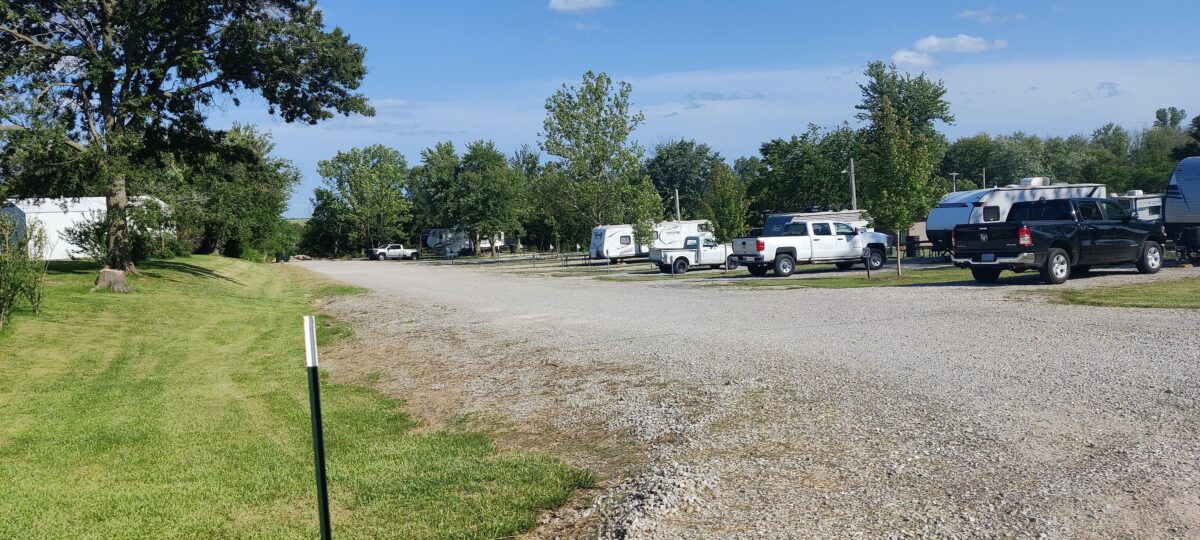 RVs and trucks parked near trees and gravel.