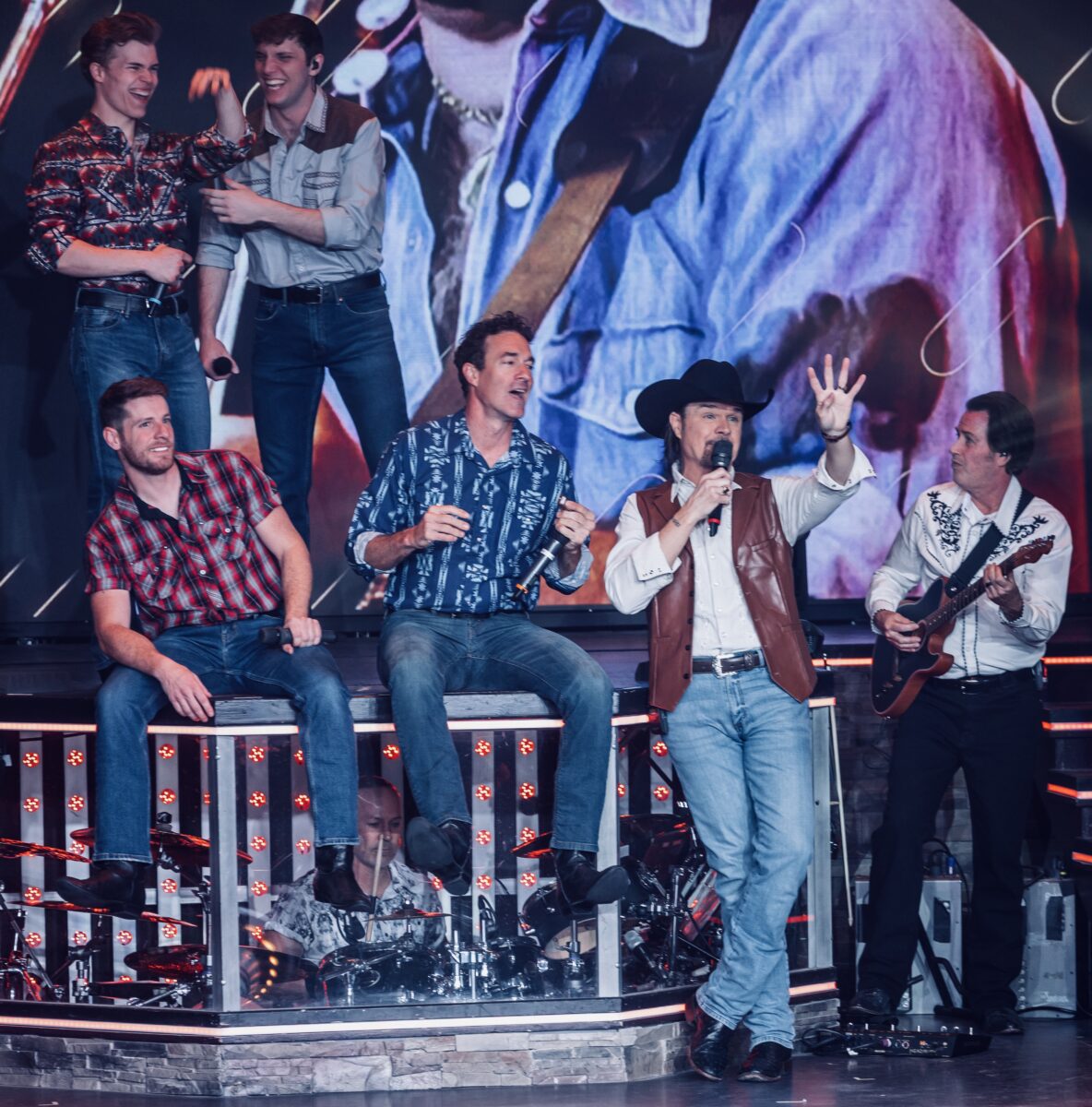 Several performers on stage before a colorful background.