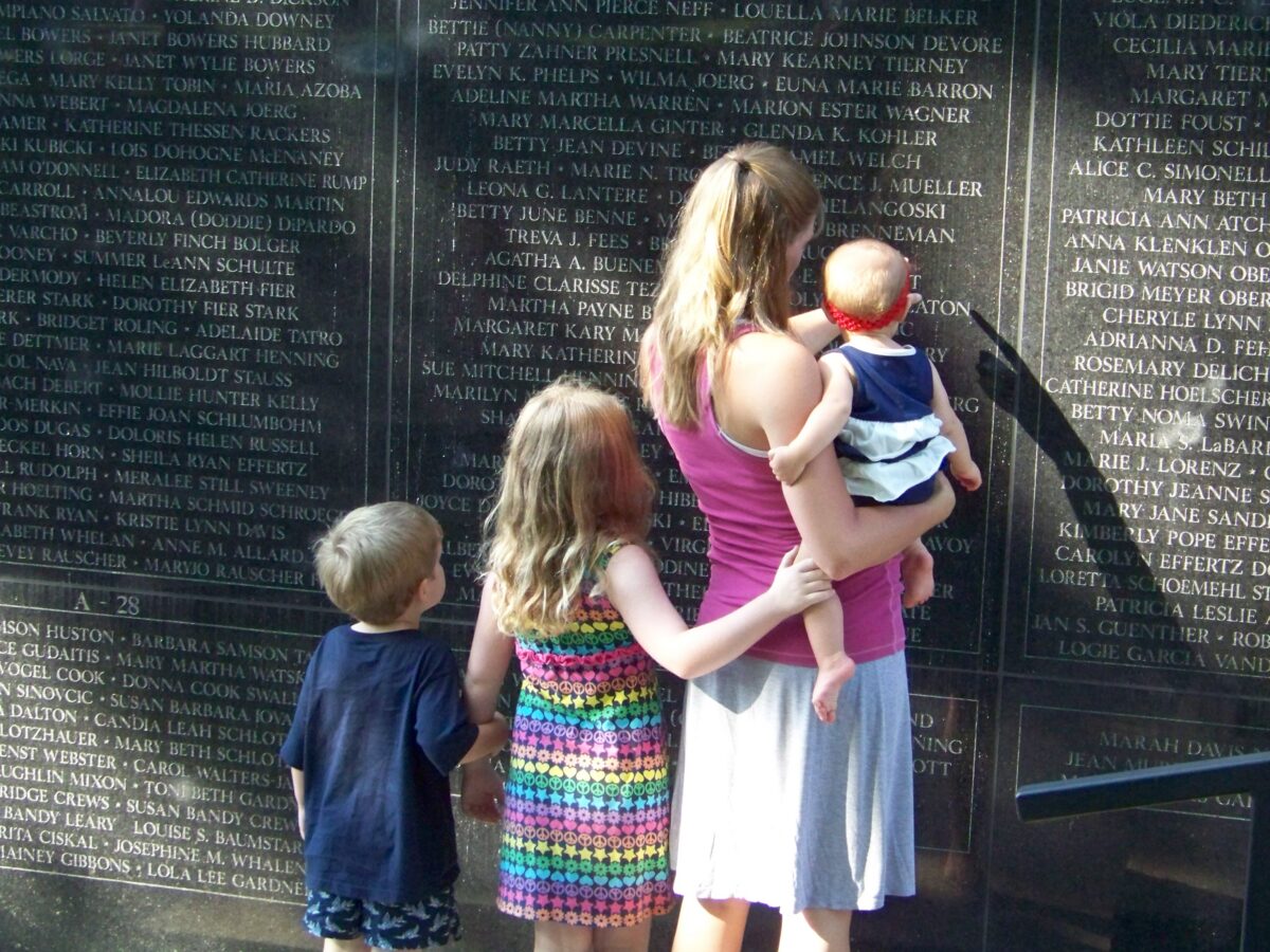 Children and a woman at a wall inscribed with the names of various mothers.