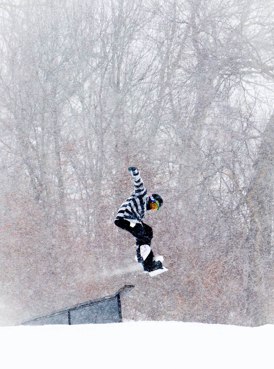 Snowboarder launches from a terrain park feature on a snowy day.