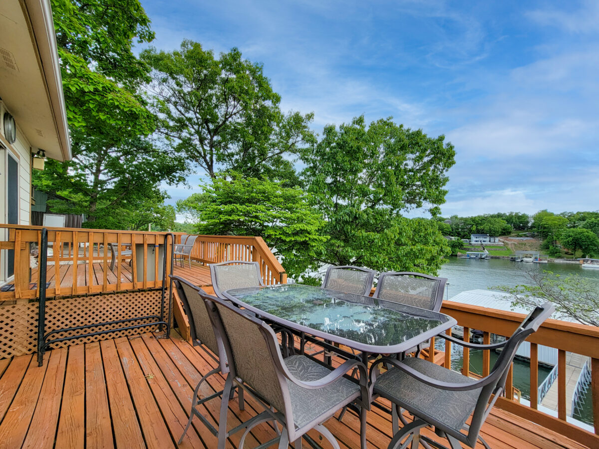 A brown patio with a table and chairs near a lake.