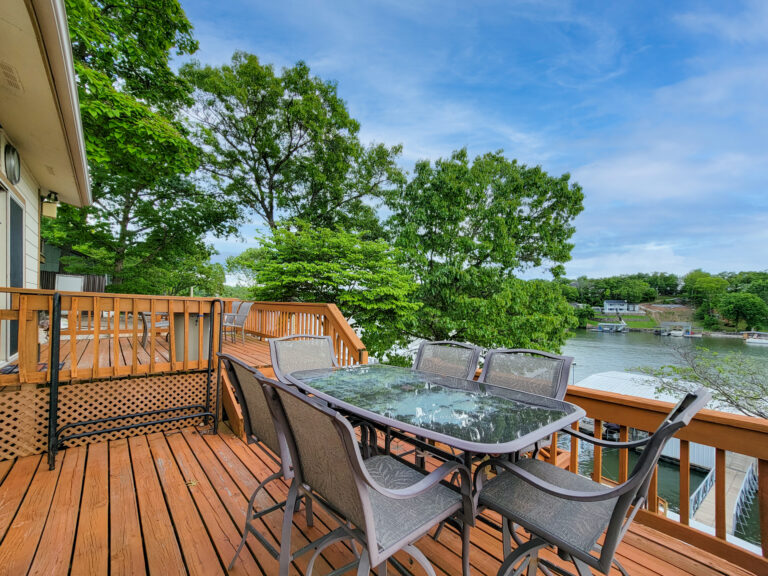 A brown patio with a table and chairs near a lake.